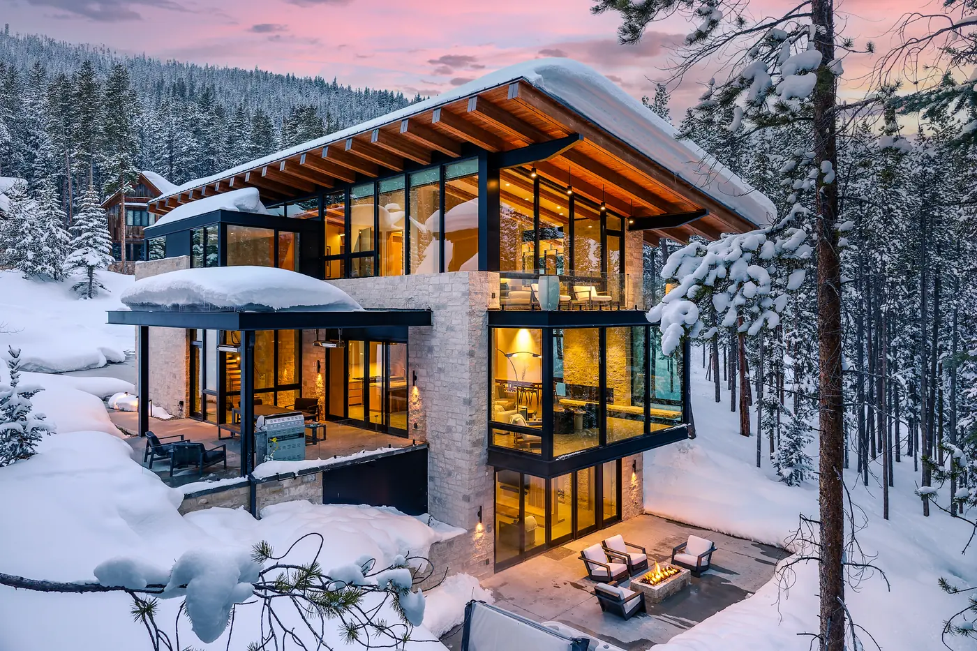 Glass-walled mountain home glowing at twilight after heavy snowfall, one of the winter markets our teams host in
