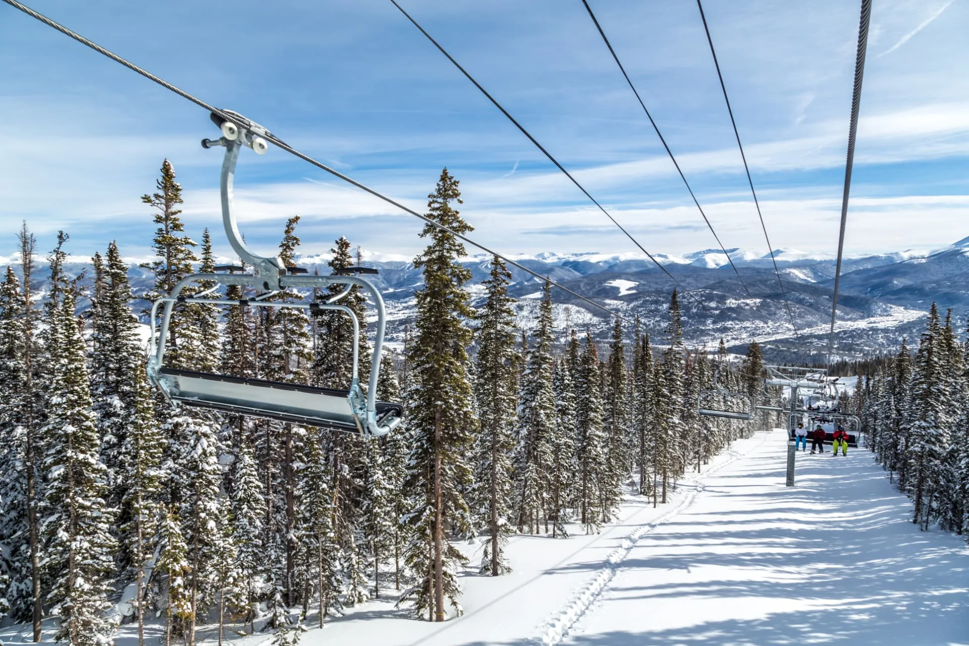 Chairlift rising over snow-covered pines with Rocky Mountain peaks beyond in Summit County, Colorado